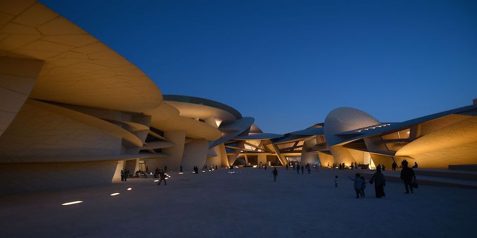 National Museum of Qatar with evening lighting, people walking outside.