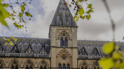 Natural History Museum Oxford - a Gothic-style building with pointed tower, framed by green leaves.
