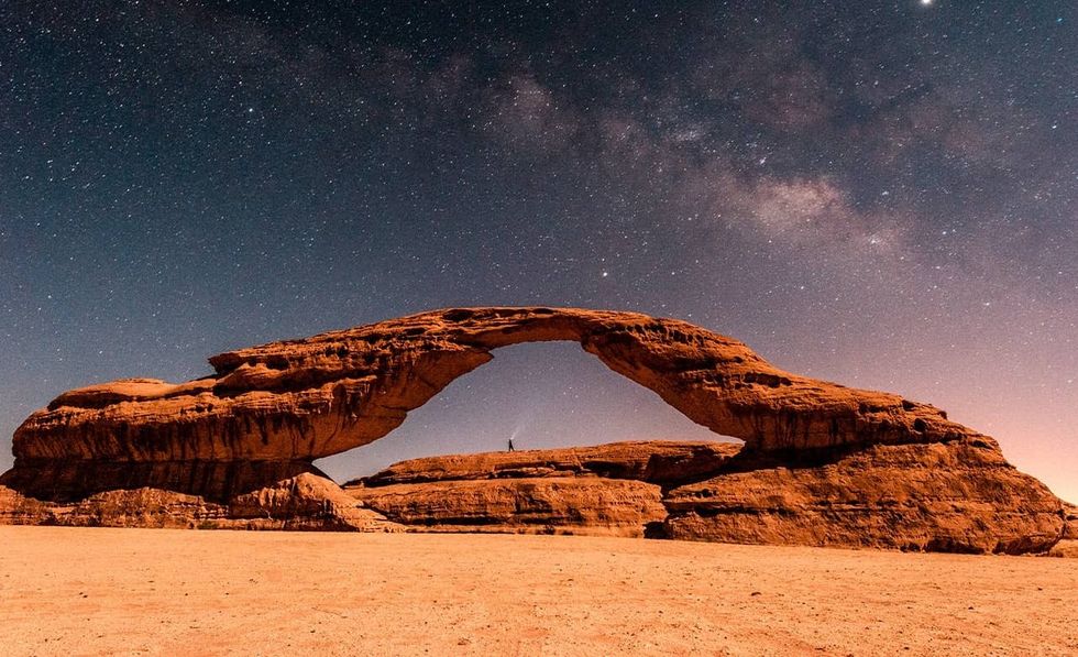 Natural rock arch under a starry night sky in a desert landscape at AlUla, Saudi Arabia