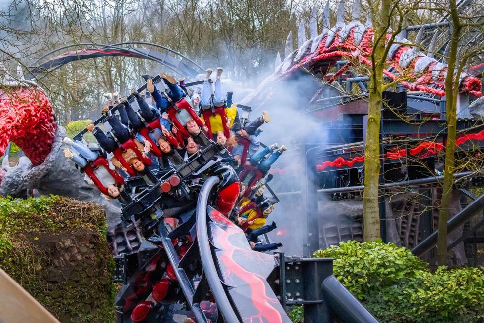 Nemesis Reborn roller coaster riders at Alton Towers upside down with red tracks and dragon-themed decor in background.