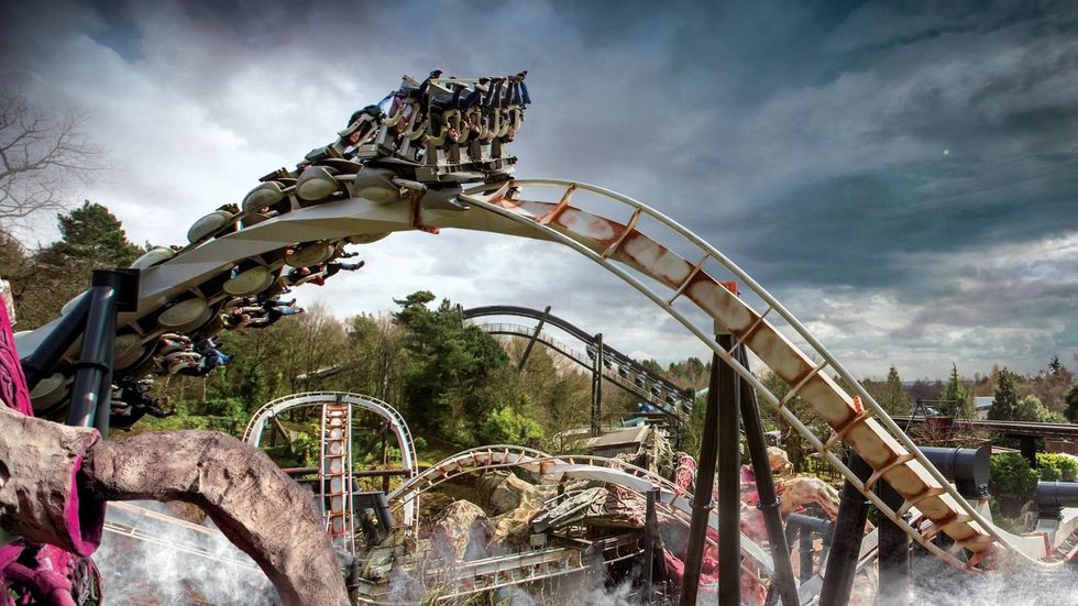 Nemesis roller coaster with passengers on a dramatic loop against a cloudy sky background.