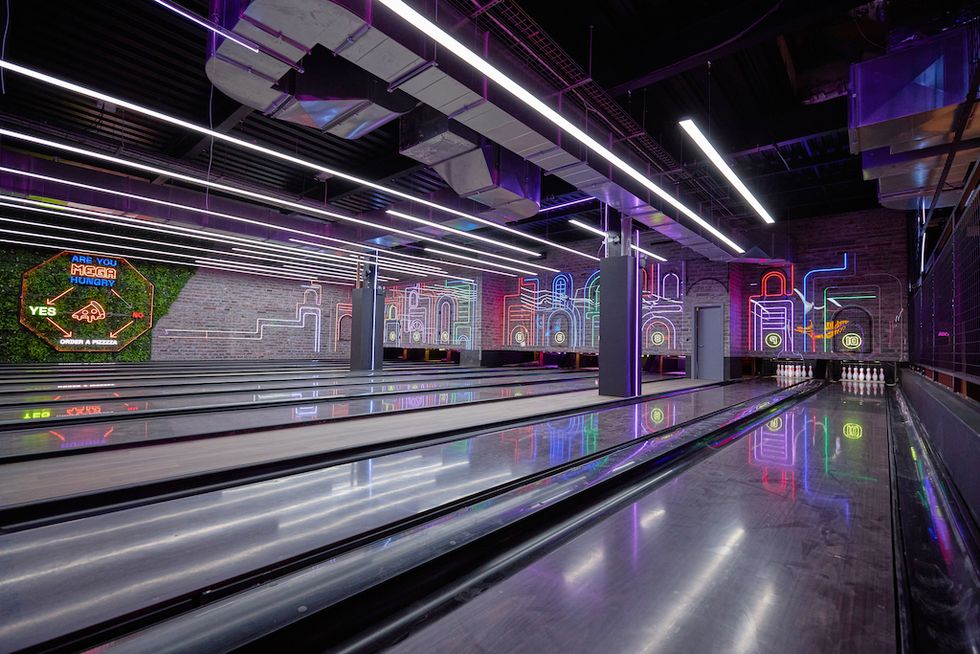 Neon-lit bowling alley with colorful wall murals and reflective lanes.