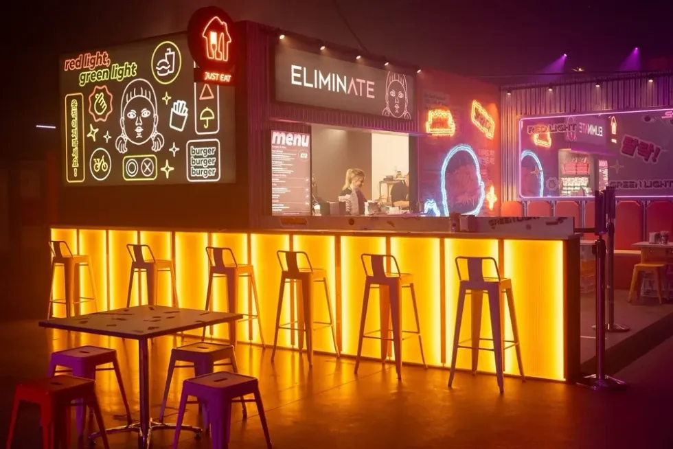 Neon-lit burger bar with stools, menu board, and vibrant signage in a moody atmosphere.