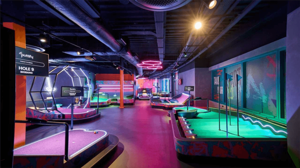 Neon-lit indoor mini-golf course with various themed holes and colorful lighting.