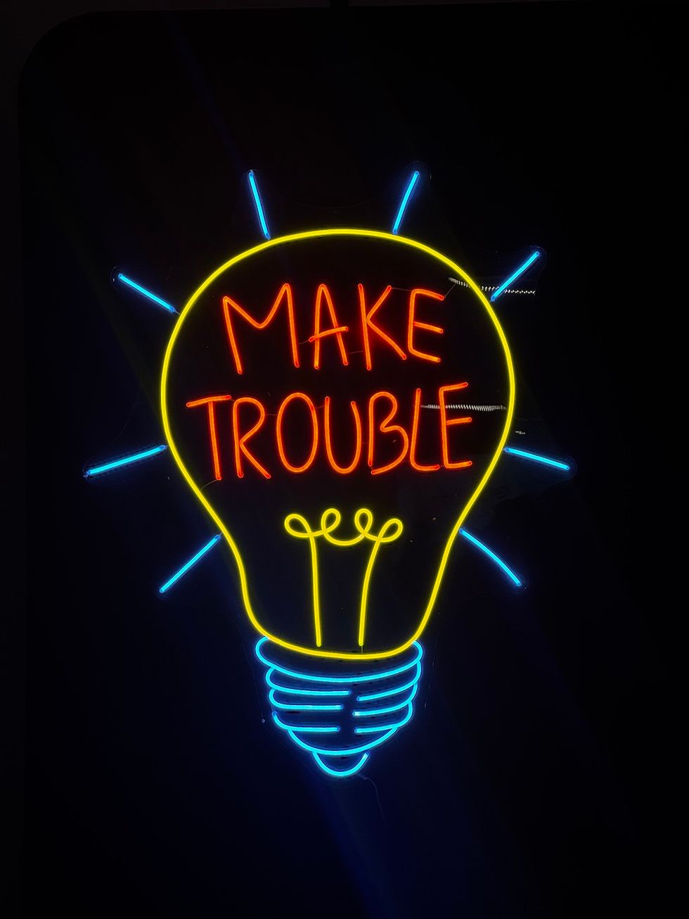 Neon sign with "MAKE TROUBLE" inside a light bulb outline.