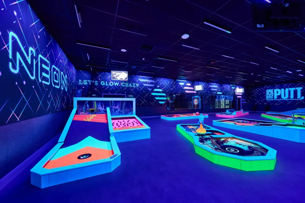 Neon-themed indoor mini golf course with glowing obstacles and vibrant colors.