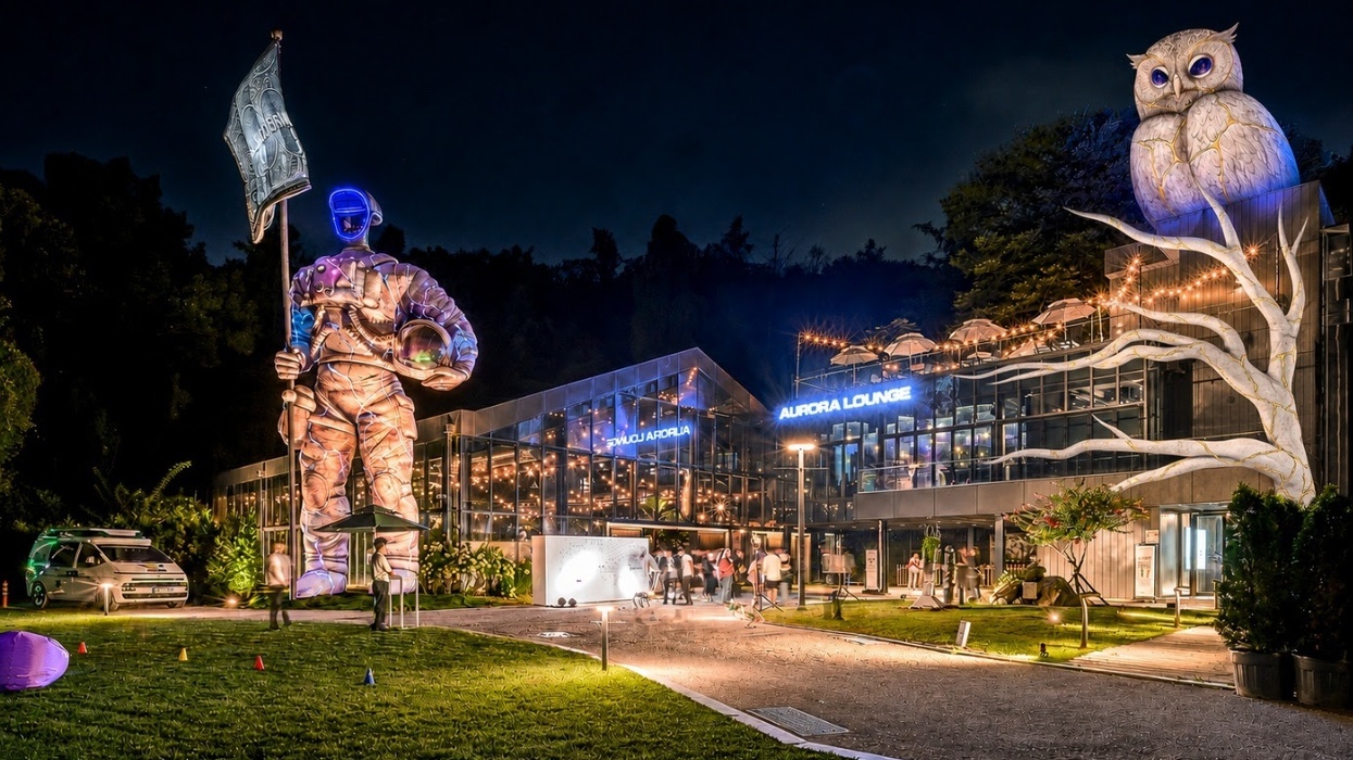 Night scene with a large astronaut statue and glowing owl by a modern glass building called Galaxy Robot Park