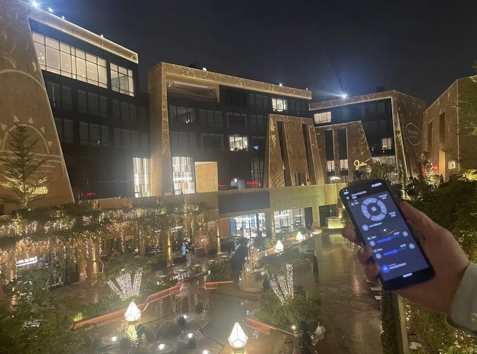 Night view of illuminated buildings at Via Riyadh with a smartphone screen in the foreground.