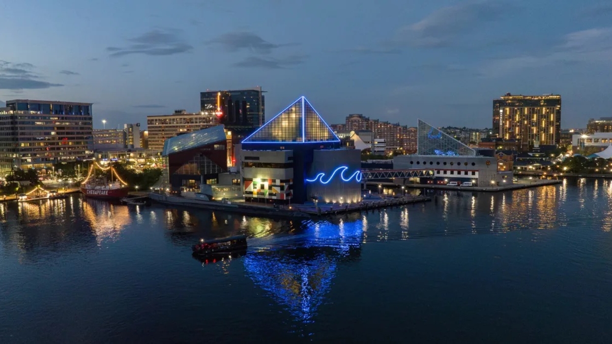 Nighttime cityscape of a waterfront with illuminated buildings including the National Aquarium and reflections.