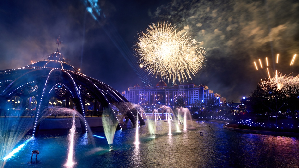 Nighttime fireworks over a lit fountain and pavilion, with a building in the background at Universal Epic Universe