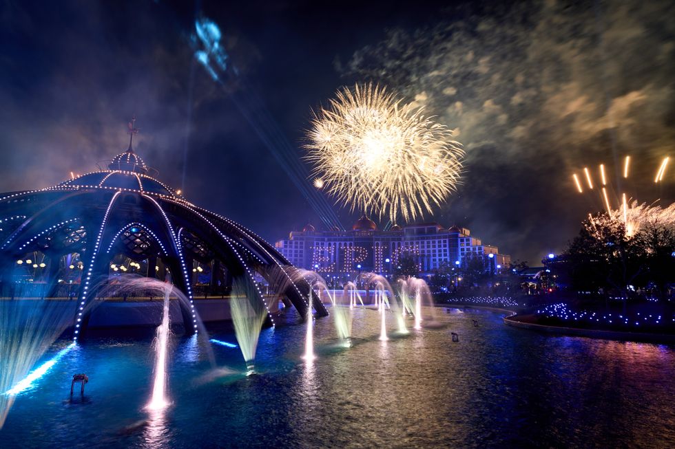 Nighttime fireworks over a lit fountain and pavilion, with a building in the background at Universal Epic Universe