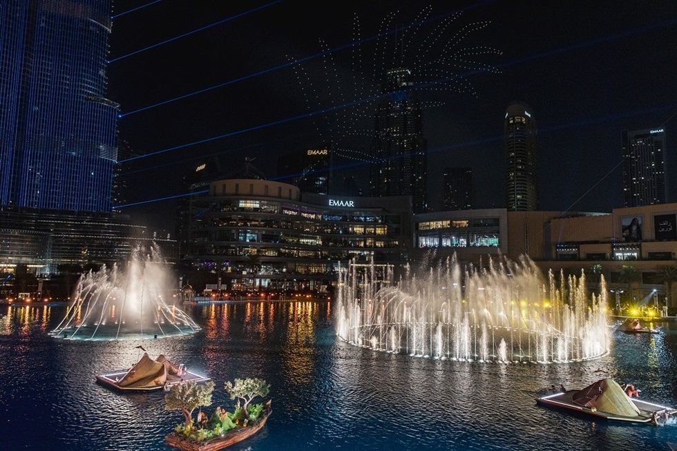 Nighttime fountain show with boats and city skyline in the background.