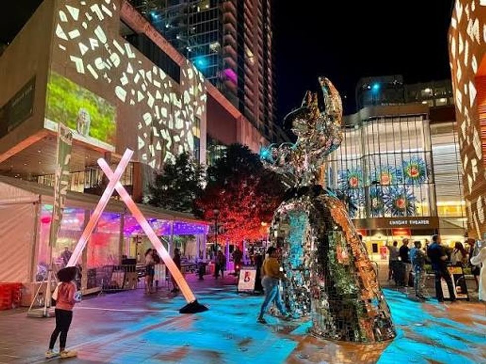 Nighttime urban scene with colorful lights and a reflective sculpture.