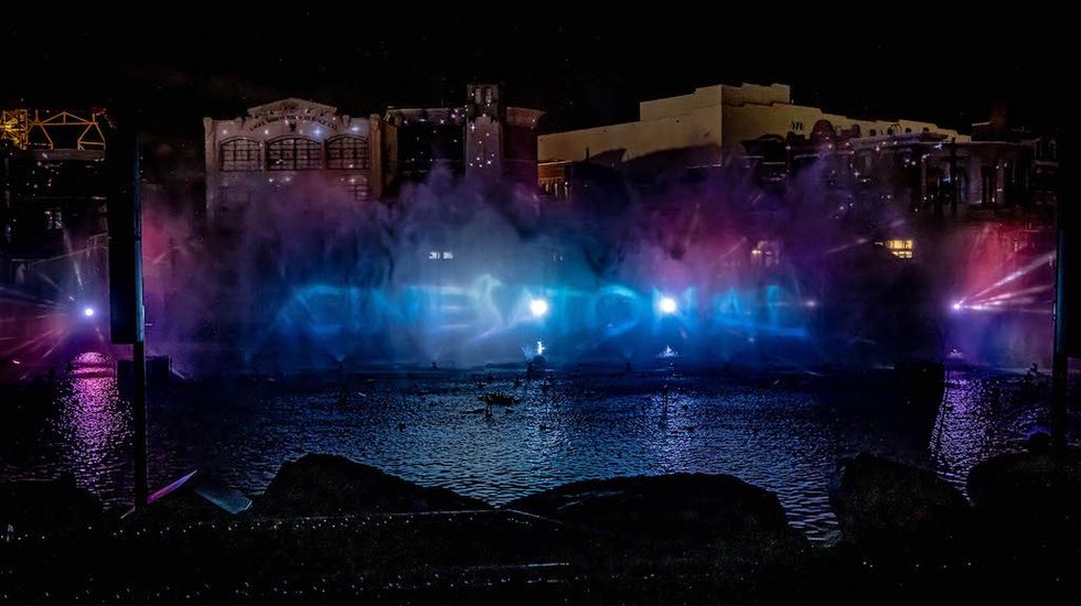 Nighttime water show with colorful lights projecting "cinematic" onto mist above water.