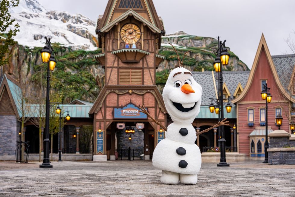 Olaf snowman character smiling in front of themed park buildings and lampposts at Disneyland Paris
