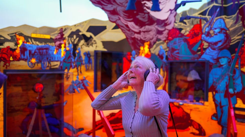 Older woman with headphones in a colorful, immersive historical exhibit. The War Rooms at The Story of Emily