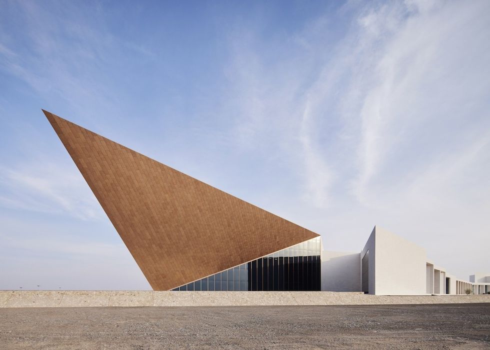 Oman Across Ages, a modern building with a large, triangular wooden roof and white walls under a blue sky.