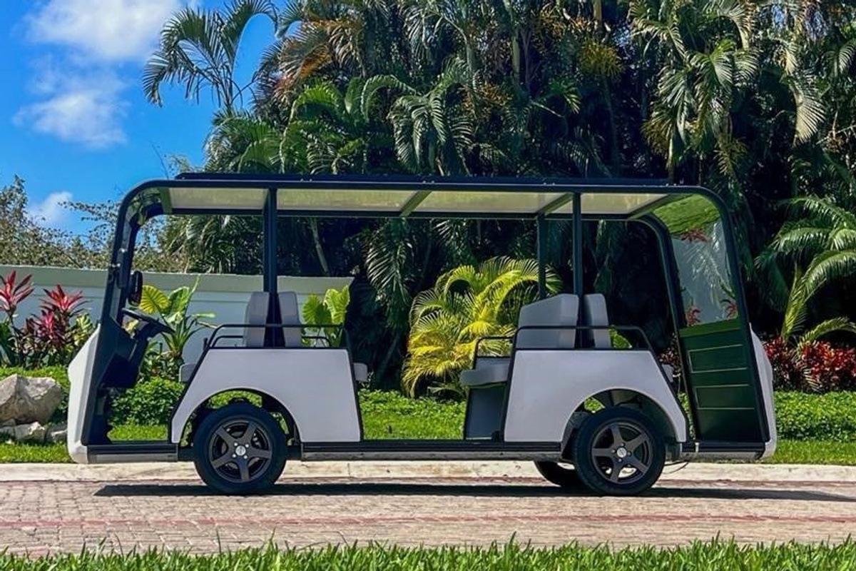 Open-air golf cart on path, surrounded by lush tropical plants and trees.