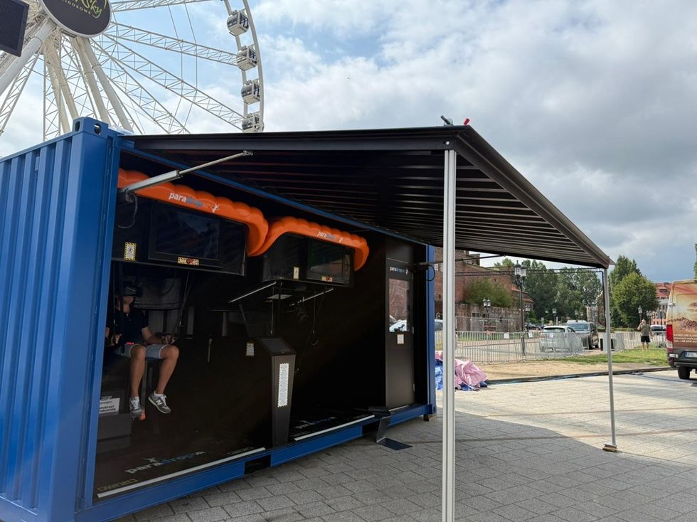 Open blue container with VR setup beside a Ferris wheel under a cloudy sky.