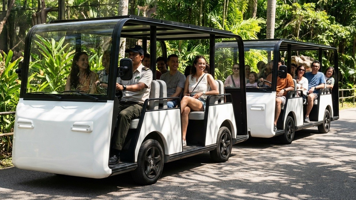 Open-sided tour tram with passengers, driving through a lush, green park.