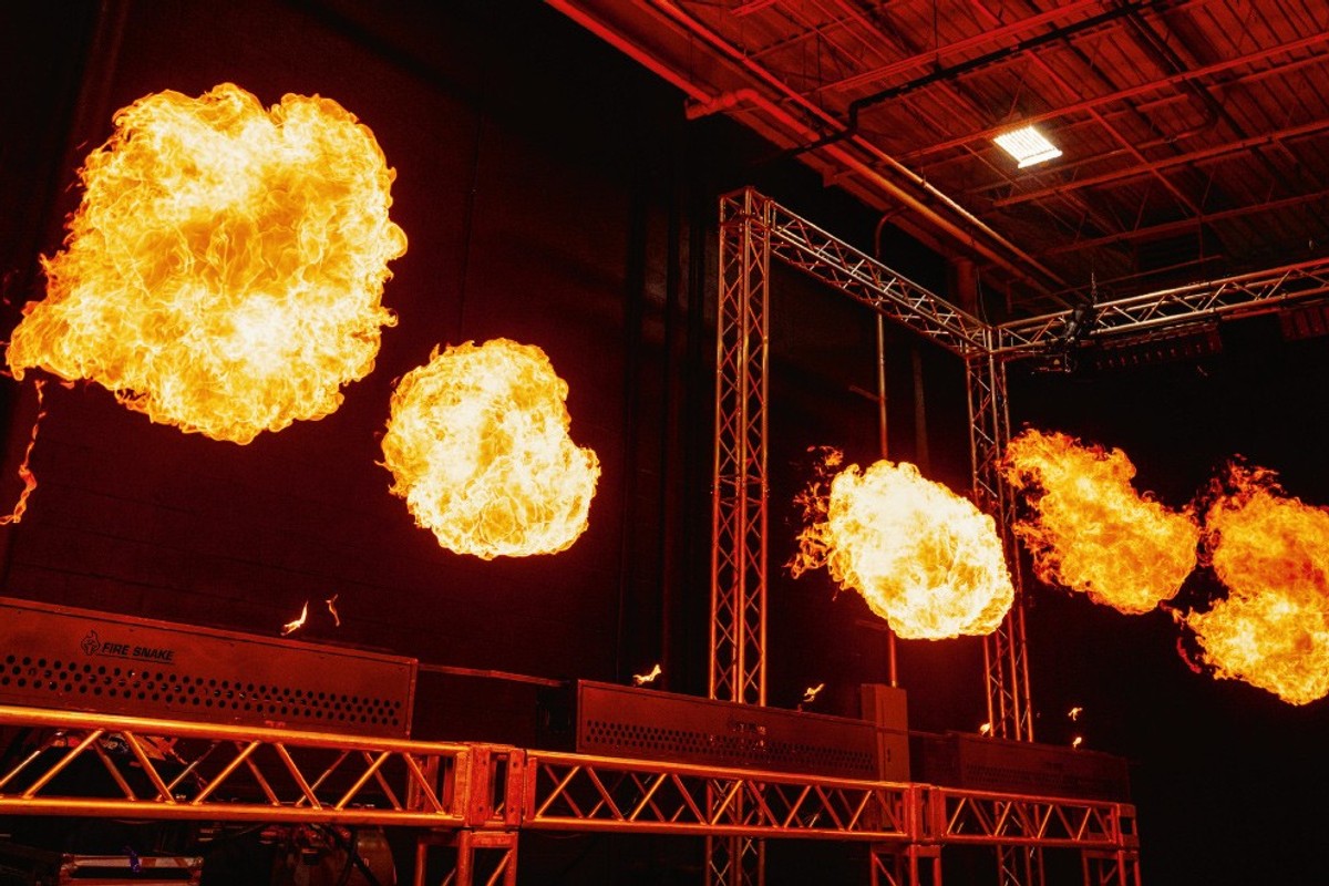 Orange fireballs in a dark room with metal stage structures.