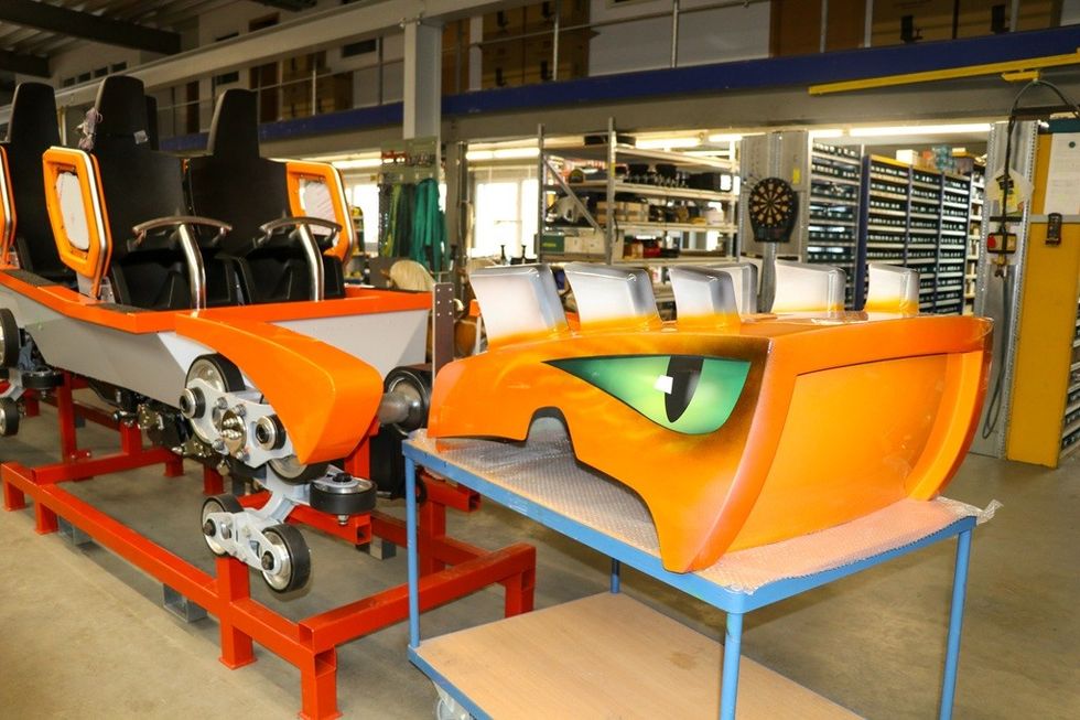 Orange roller coaster cars in a workshop.