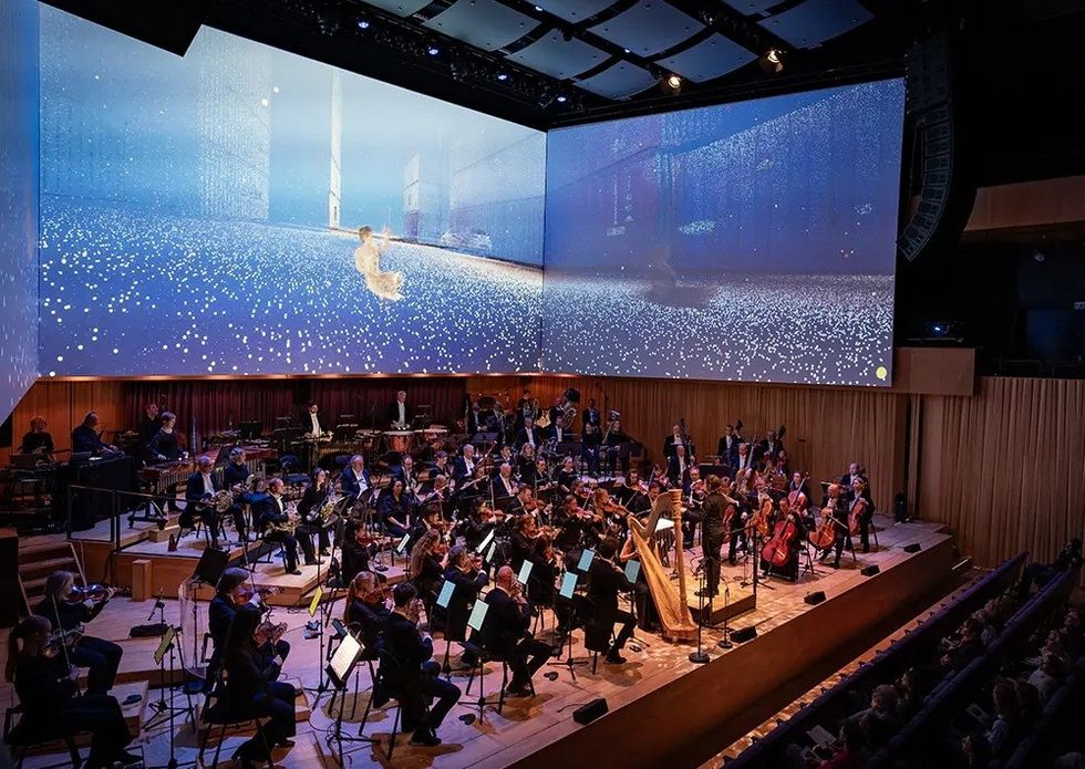 Orchestra performing on stage with large digital display of stars and figure in motion.