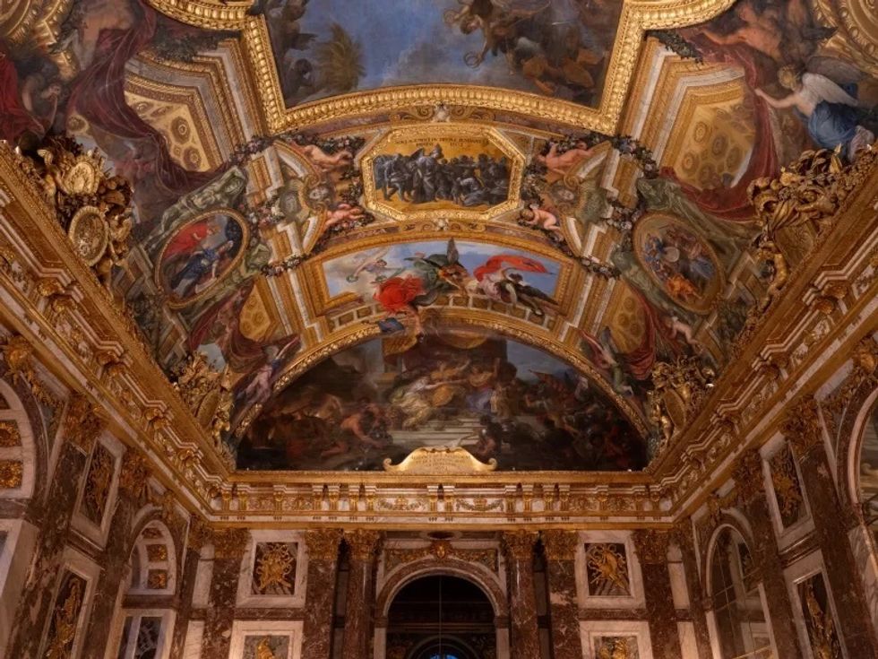 Ornate ceiling with detailed frescoes in a grand, richly decorated room at Ch\u00e2teau de Versailles