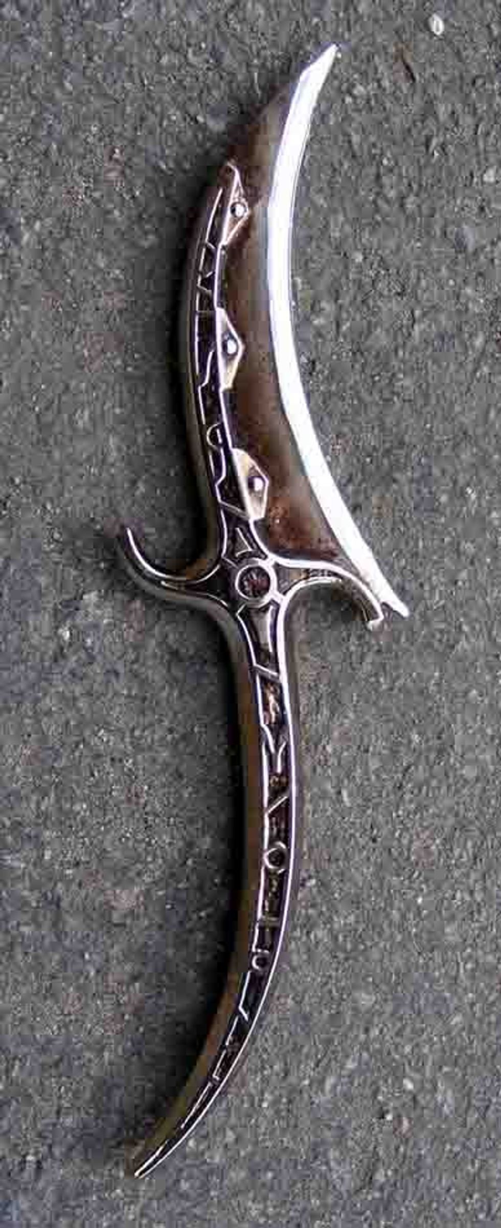 Ornate crescent-shaped dagger with engraved designs on a textured gray background.