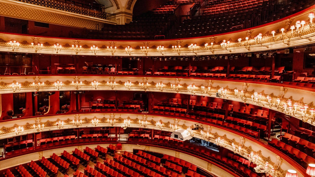 Ornate, empty theater interior with red seats and glowing chandeliers.