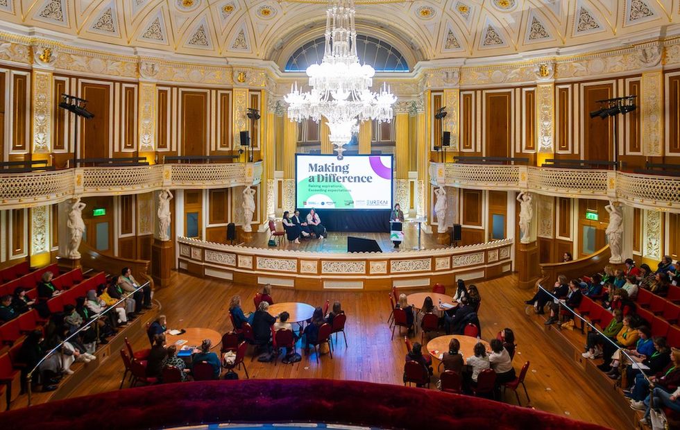 Ornate hall with an audience, stage, and "Making a Difference" displayed on screen.