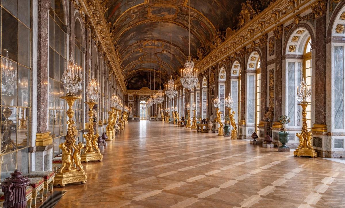 Ornate hall with chandeliers, mirrored walls, and arched windows.