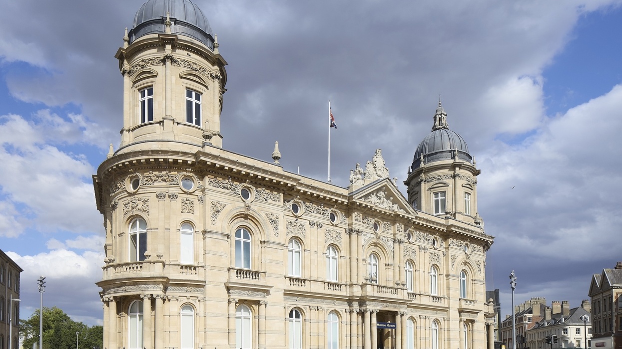 Ornate historic building containing Hull Maritime Museum with two domes under a cloudy sky, people walking nearby