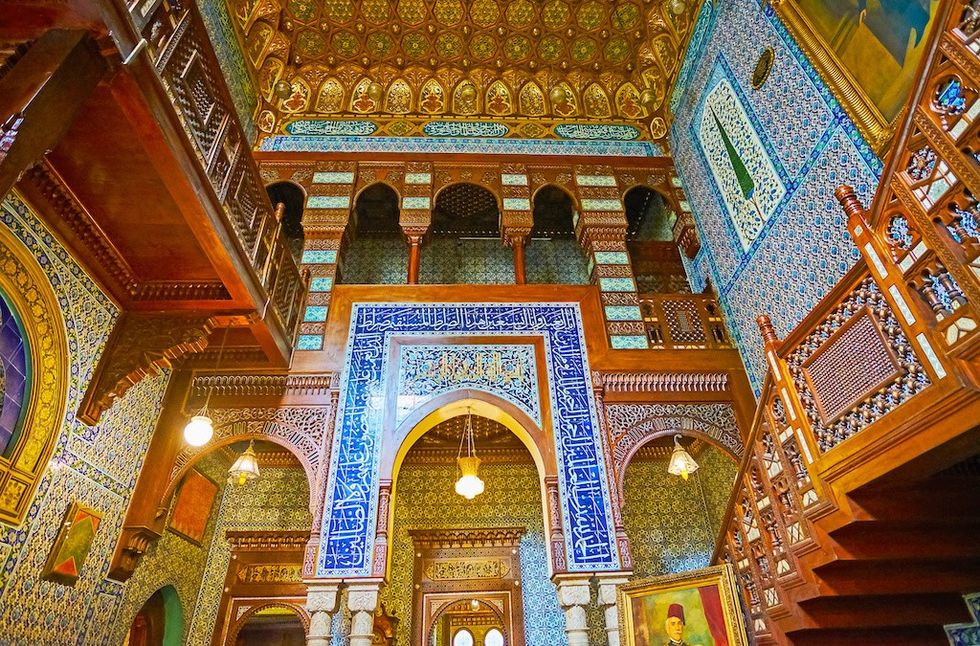 Ornate interior with intricate tile patterns, arches, and a wooden staircase at the Manial Palace Museum, Cairo