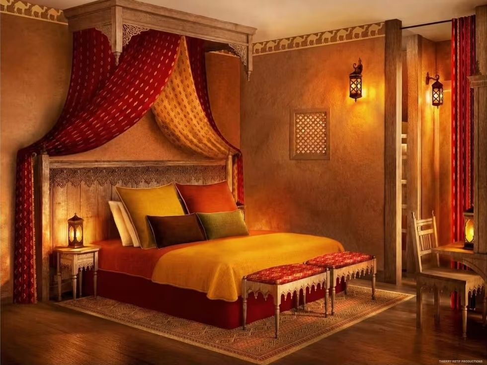 Ornate Moroccan-style hotel room at Parc Asterix with a draped canopy bed, warm lanterns, and rich red and gold decor.