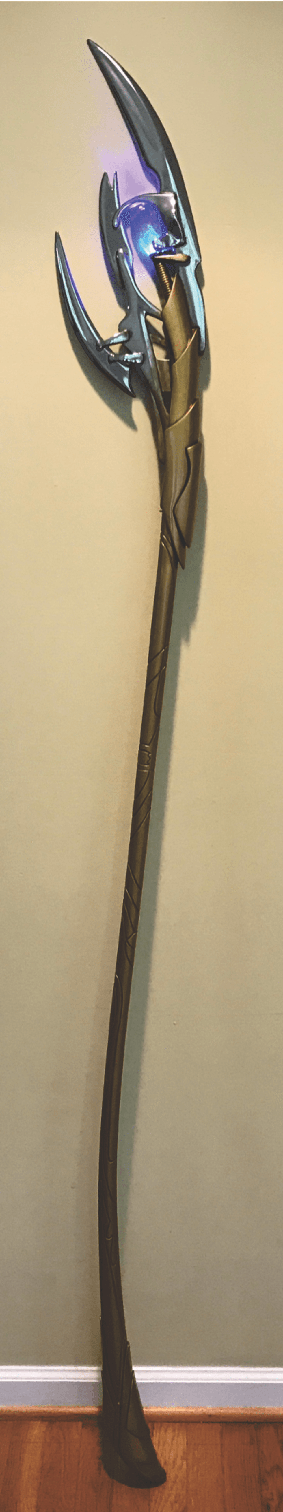 Ornate staff with glowing purple blade on a wooden floor background.