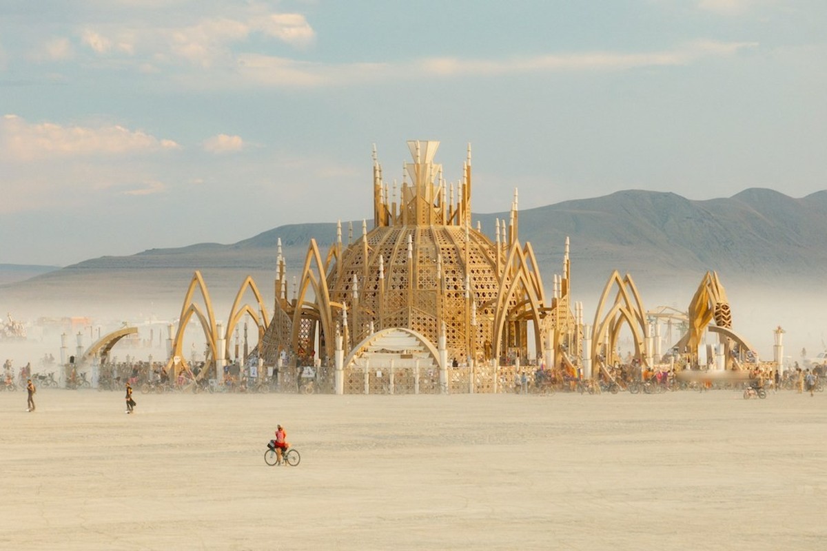 Ornate structure at desert festival with mountains and scattered people on bikes. The Temple at Burning Man