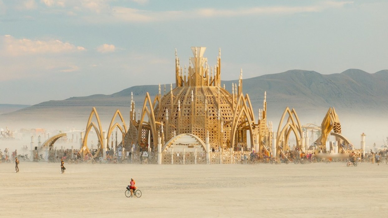 Ornate structure at desert festival with mountains and scattered people on bikes. The Temple at Burning Man