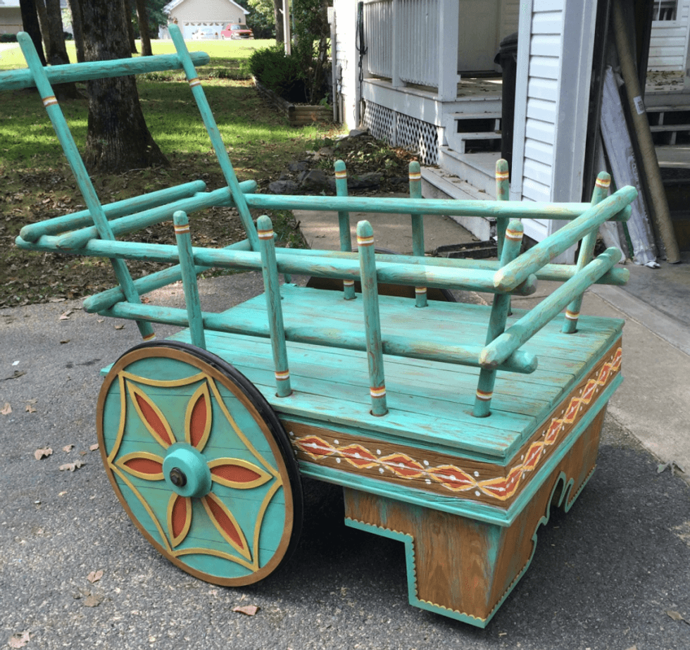 Ornate teal wooden wagon with decorative wheels on a driveway.