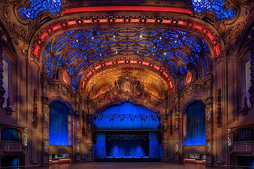 Ornate theater interior with vibrant blue and red lighting and intricate ceiling details.