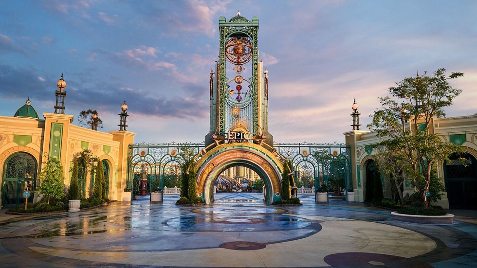 Ornate theme park entrance of Universal Epic Universe under a colorful sky at sunrise or sunset.