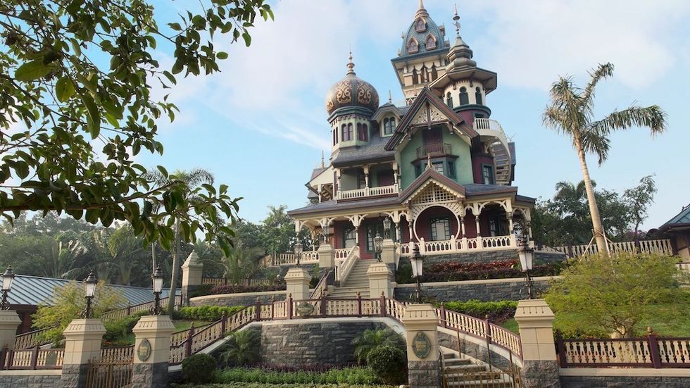 Ornate Victorian mansion with domes, surrounded by lush greenery and palm trees. \u200bMystic Manor - Hong Kong Disneyland