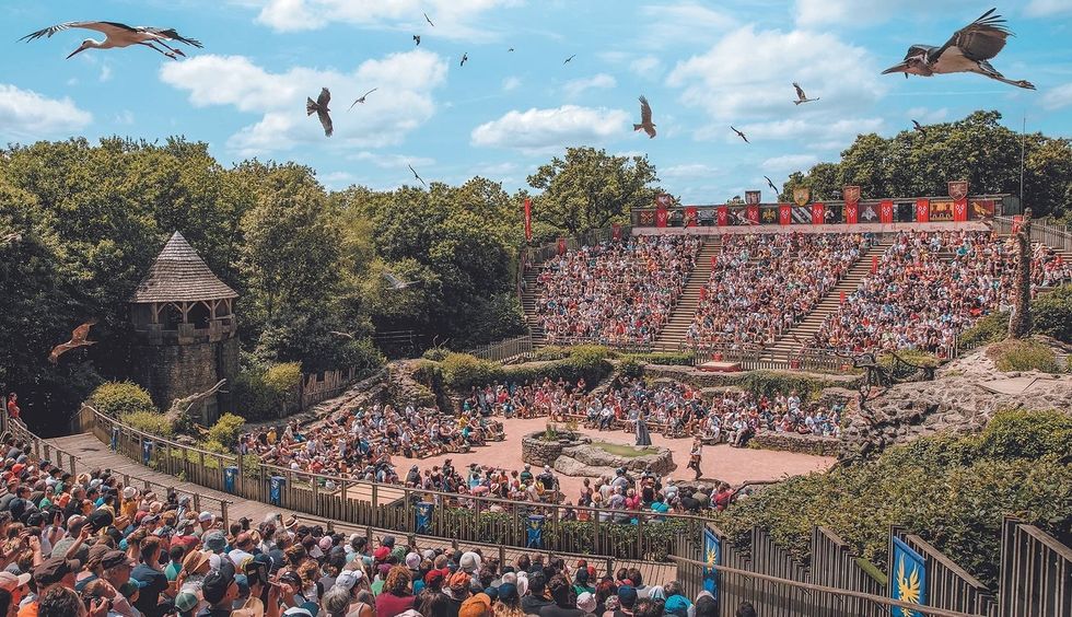 Outdoor amphitheater show at Puy du Fou with a large audience and birds flying above.