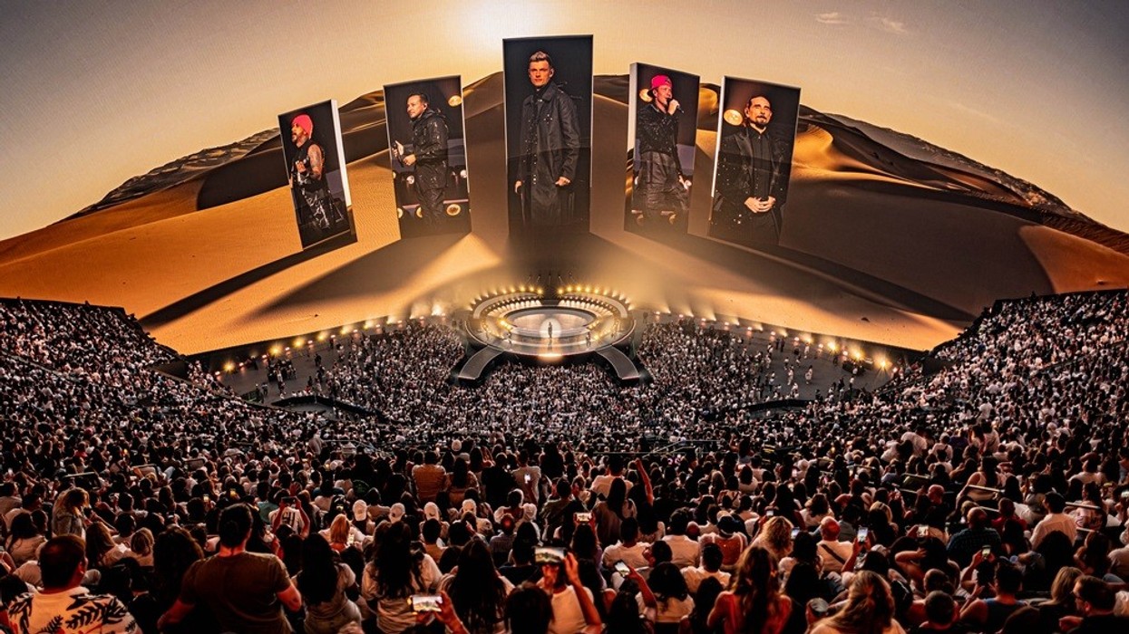 Outdoor concert in a large amphitheater, featuring holograms and a vast desert backdrop.