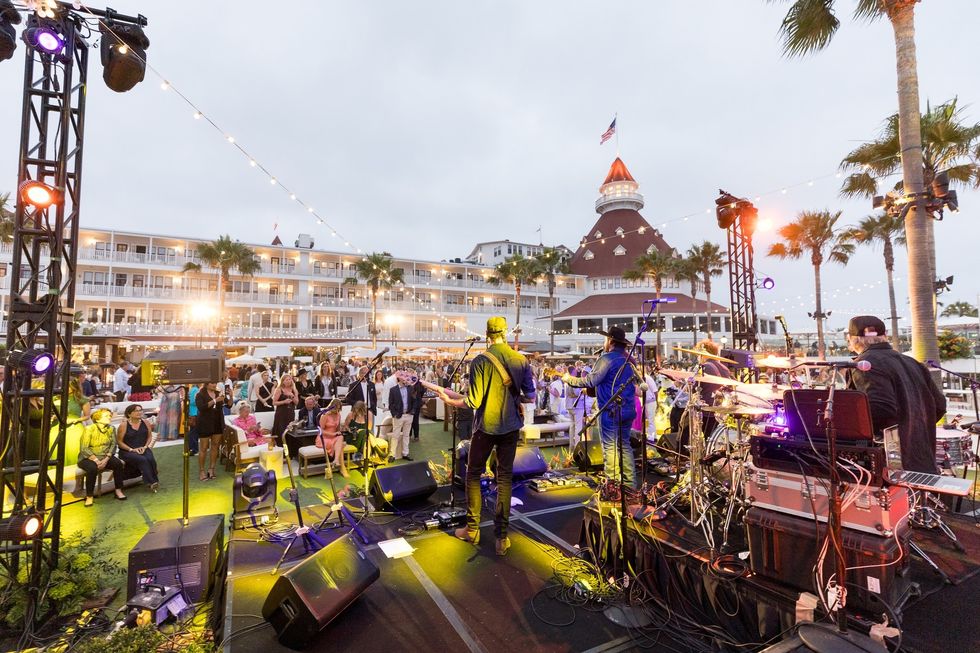 Outdoor concert with band playing to a lively crowd, historic hotel in the background.