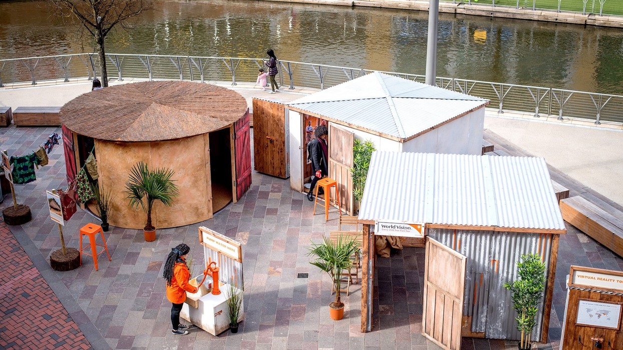 Outdoor exhibit with huts by a river, featuring signs and interactive displays.