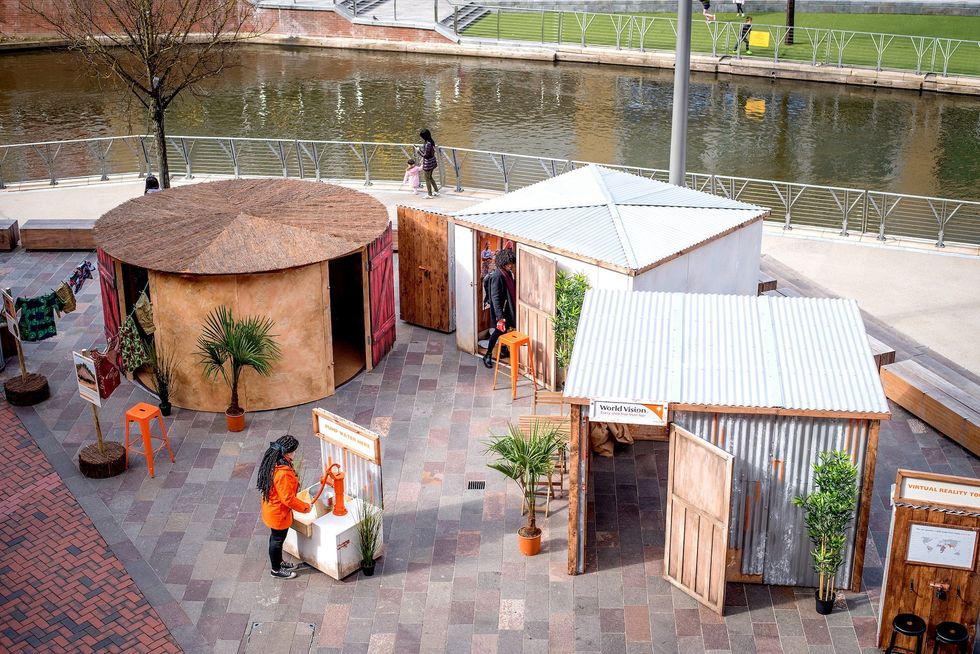 Outdoor exhibit with huts by a river, featuring signs and interactive displays.