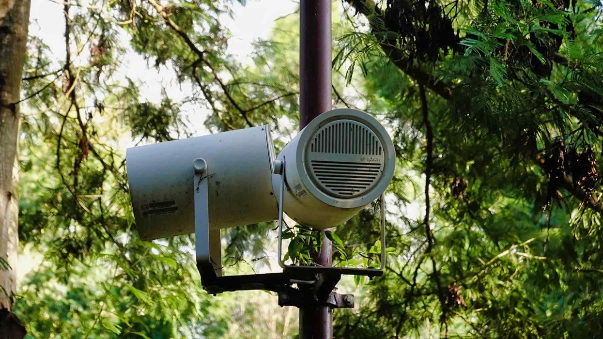 Outdoor speaker on a pole among lush green trees.