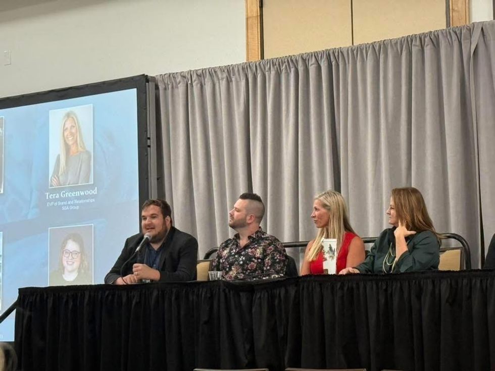 Panel discussion with four people seated at a table, one speaking into a microphone.