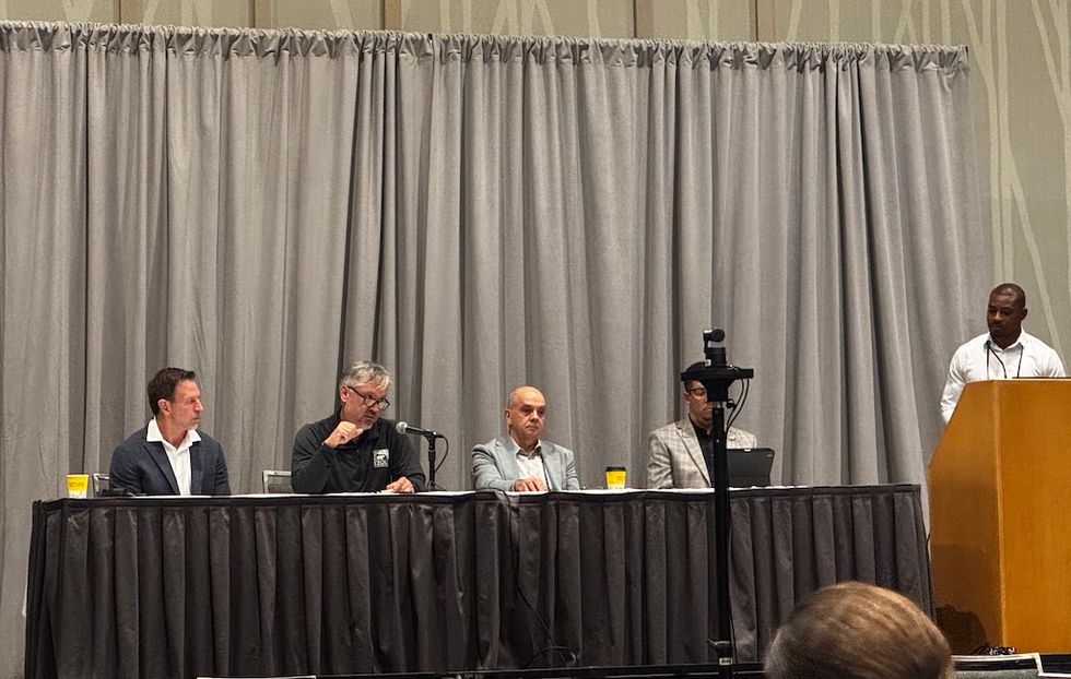 Panel discussion with four seated speakers and one standing at a podium.
